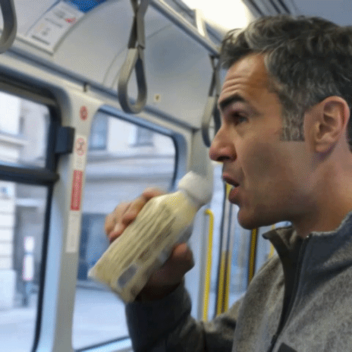 Person in einer Straßenbahn beißt in ein in Papier eingewickeltes Baguette