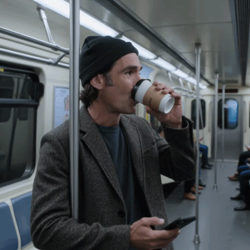 Person in einer U-Bahn trinkt aus einem Coffee-to-go-Becher und hält ein Smartphone in der Hand