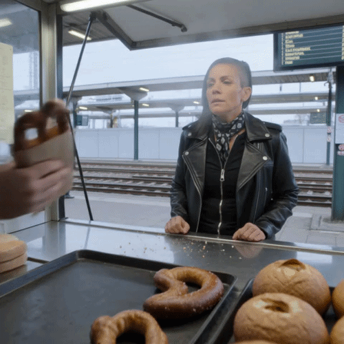 An einem Backwaren-Stand am Bahnsteig wird eine Brezel über die Theke gereicht