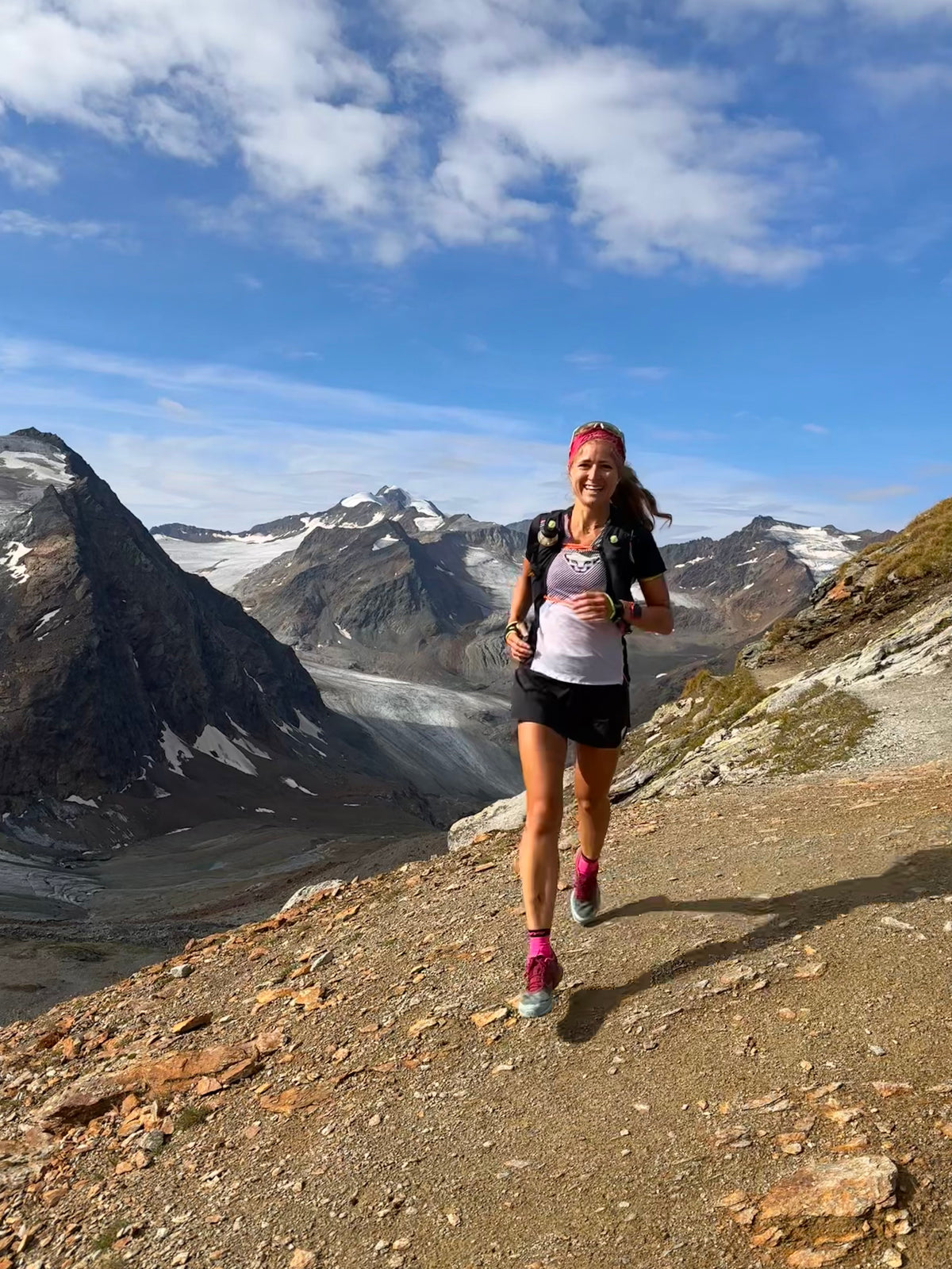 Person läuft auf einem schmalen Bergpfad, im Hintergrund Gletscher und schneebedeckte Gipfel