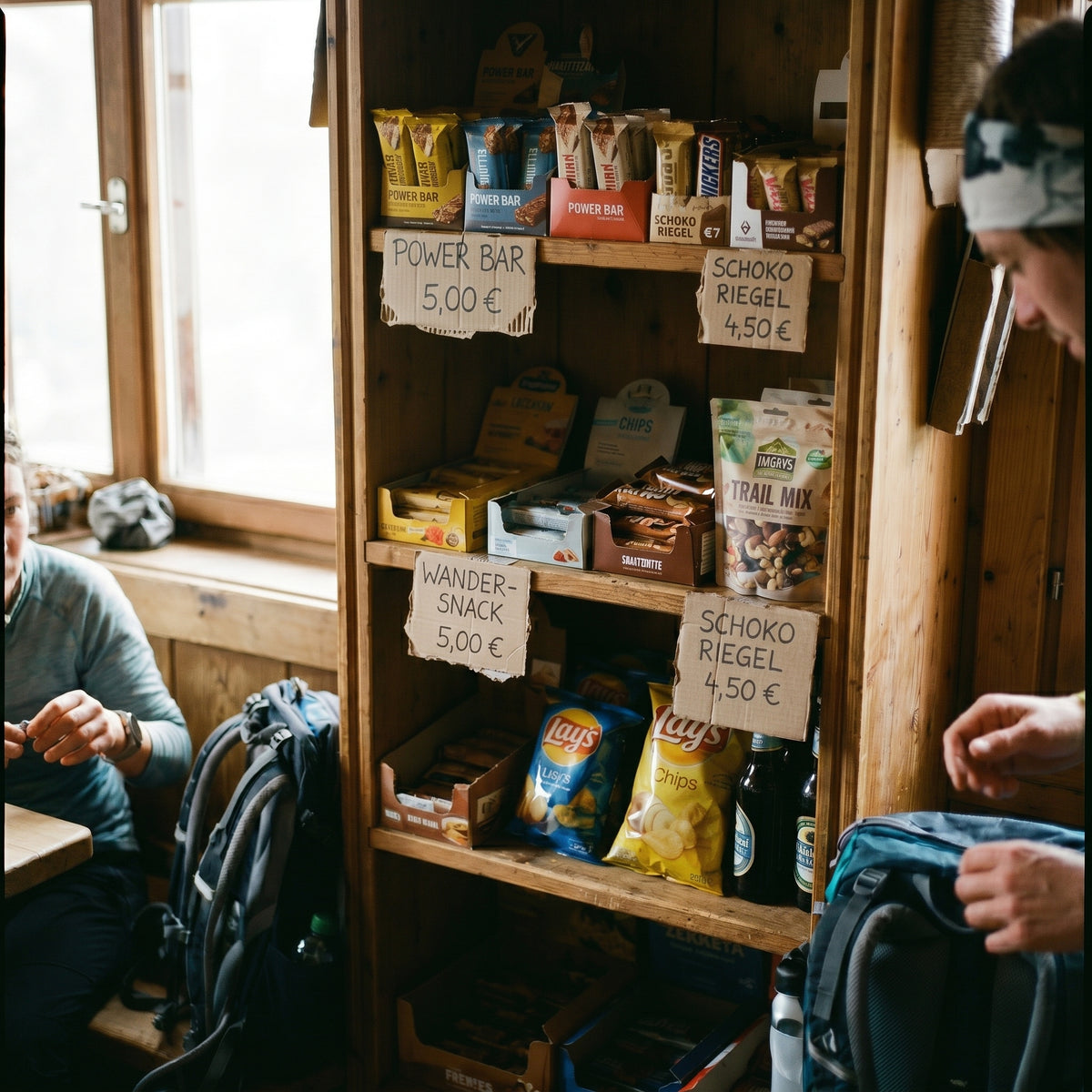 Verkaufsregal in einer Berghütte mit handgeschriebenen Preisschildern: Power Bar 5,00 Euro, Schoko Riegel 4,50 Euro, Wander-Snack 5,00 Euro