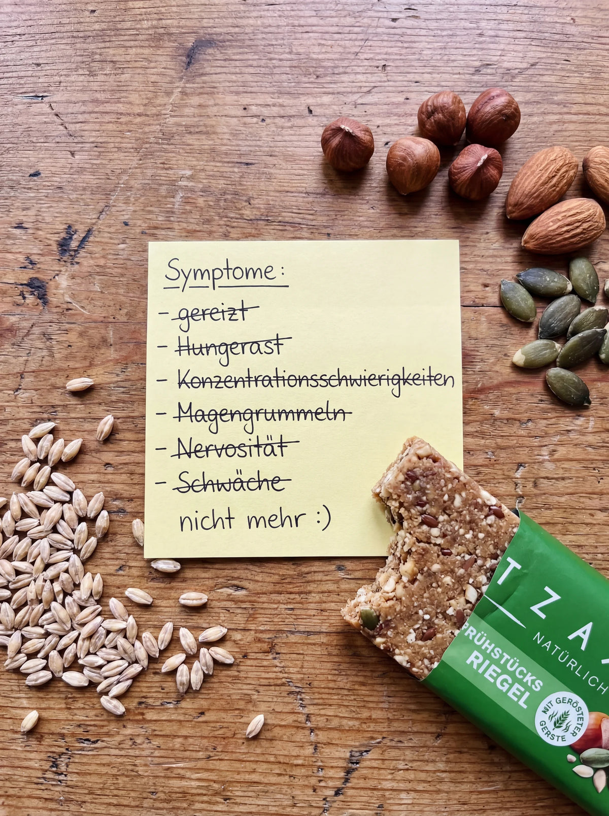 Notizzettel mit durchgestrichener Symptomliste und dem Zusatz „nicht mehr :)“, daneben ein angebrochener TZAMPAS Frühstücksriegel