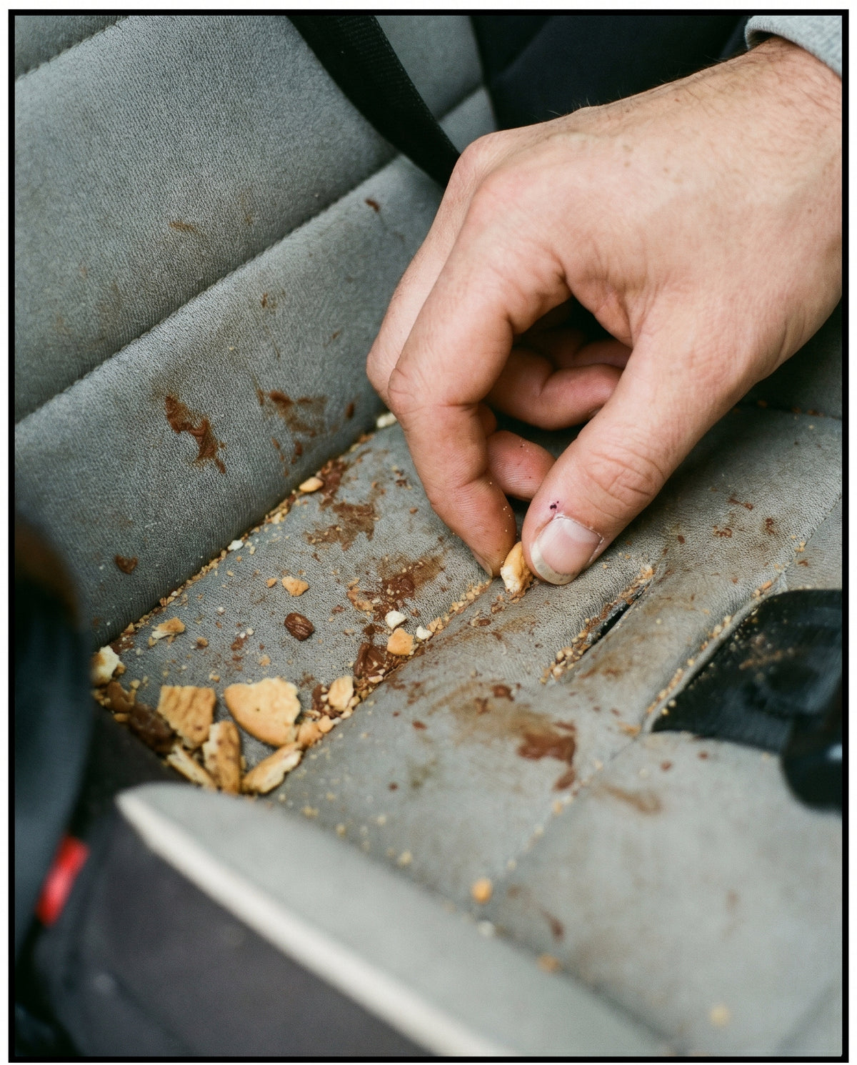 Hand sammelt Krümel von einem verschmutzten Autositz, überall Schokoladenflecken