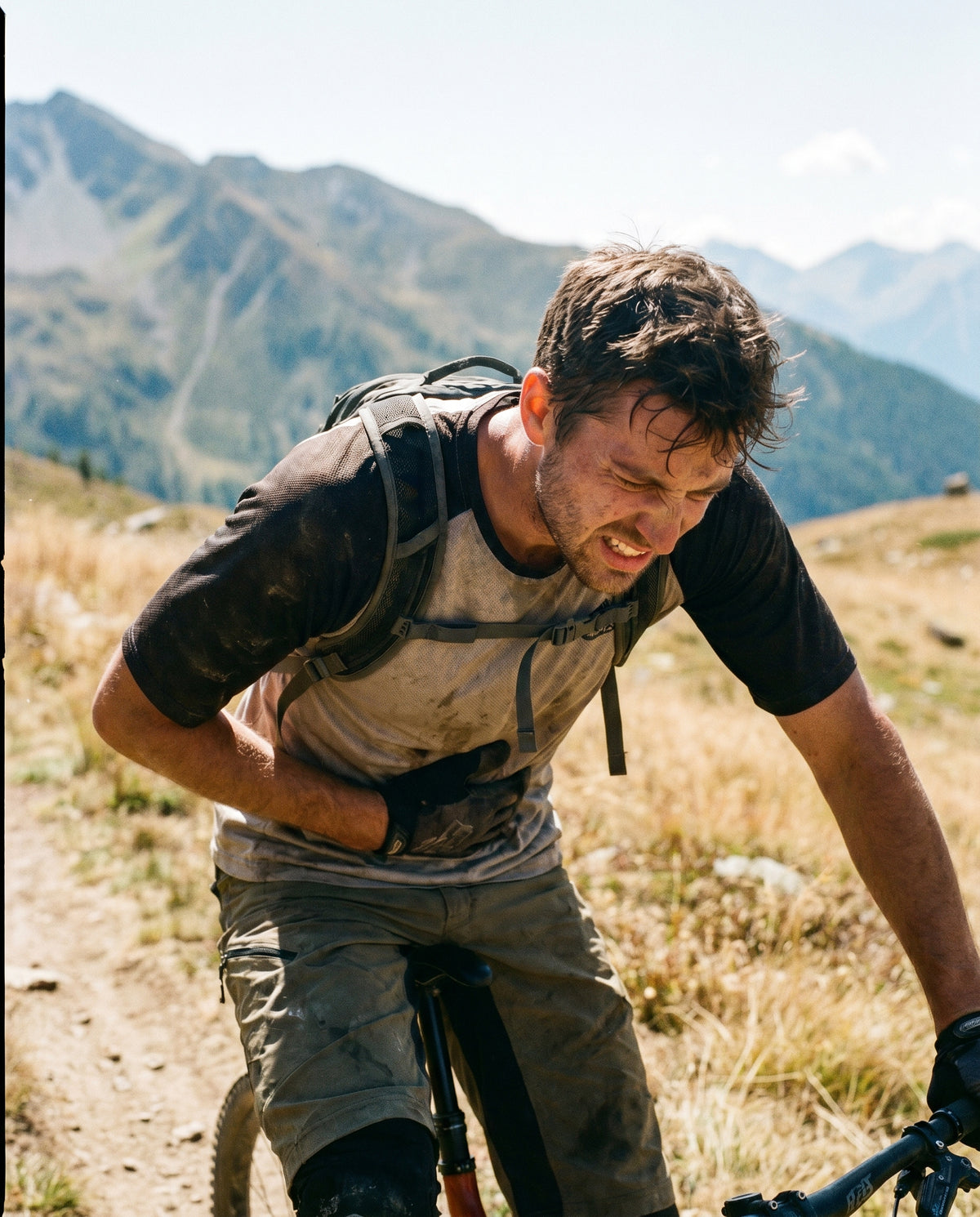 Person stützt sich schwer atmend auf den Lenker eines Mountainbikes, im Hintergrund eine Berglandschaft